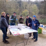 A group of volunteers standing around tables set up with trays and sampling equipment during an extended Riverfly survey under a viaduct.
