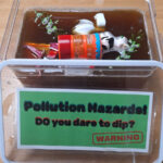 A clear plastic tub filled with murky brown water and toy items representing river pollutants, used as DCRT’s ‘pollution tank’ educational game.