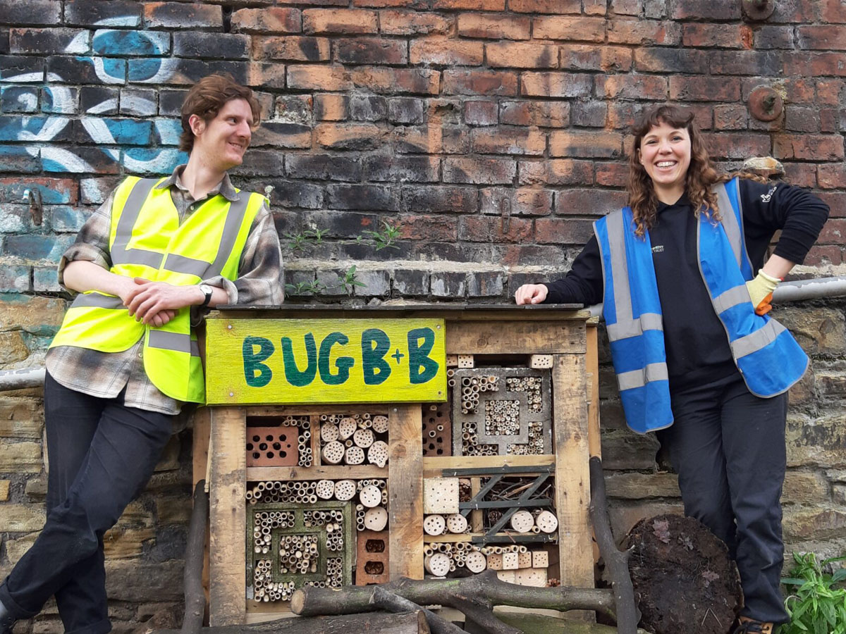 Two volunteers standing beside a community-built bug hotel as part of the All Hands on the Don project.