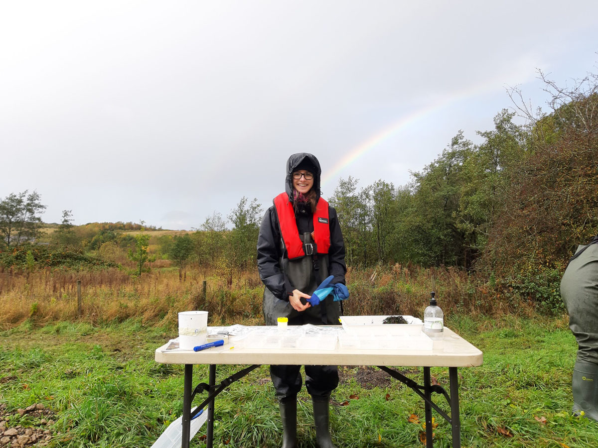 Volunteer in waterproof clothing standing at an outdoor table preparing equipment for a river survey.