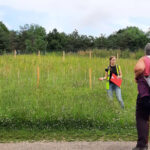 An outdoor education session with a group listening to a guide in a meadow beside the river.