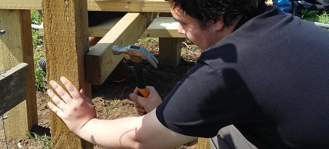 A volunteer using a hammer to install a wooden post during a practical conservation task.