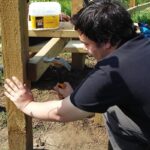 A volunteer using a hammer to install a wooden post during a practical conservation task.