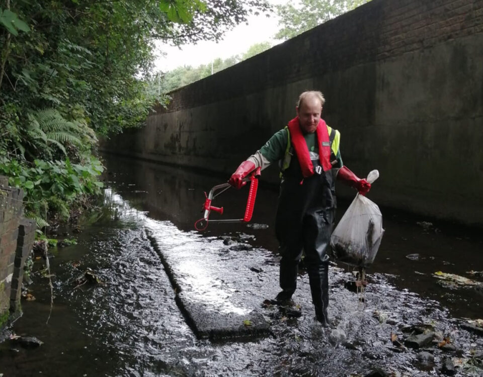 A volunteer wearing protective gear removing litter from a river channel.