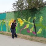 A volunteer standing beside a colourful mural created as part of a riverside community art project.